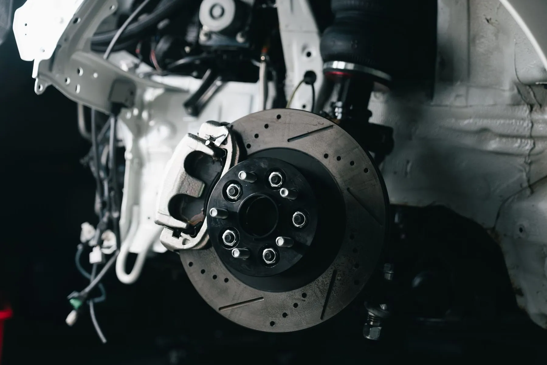 A drilled brake disc and caliper on a car with the wheel removed