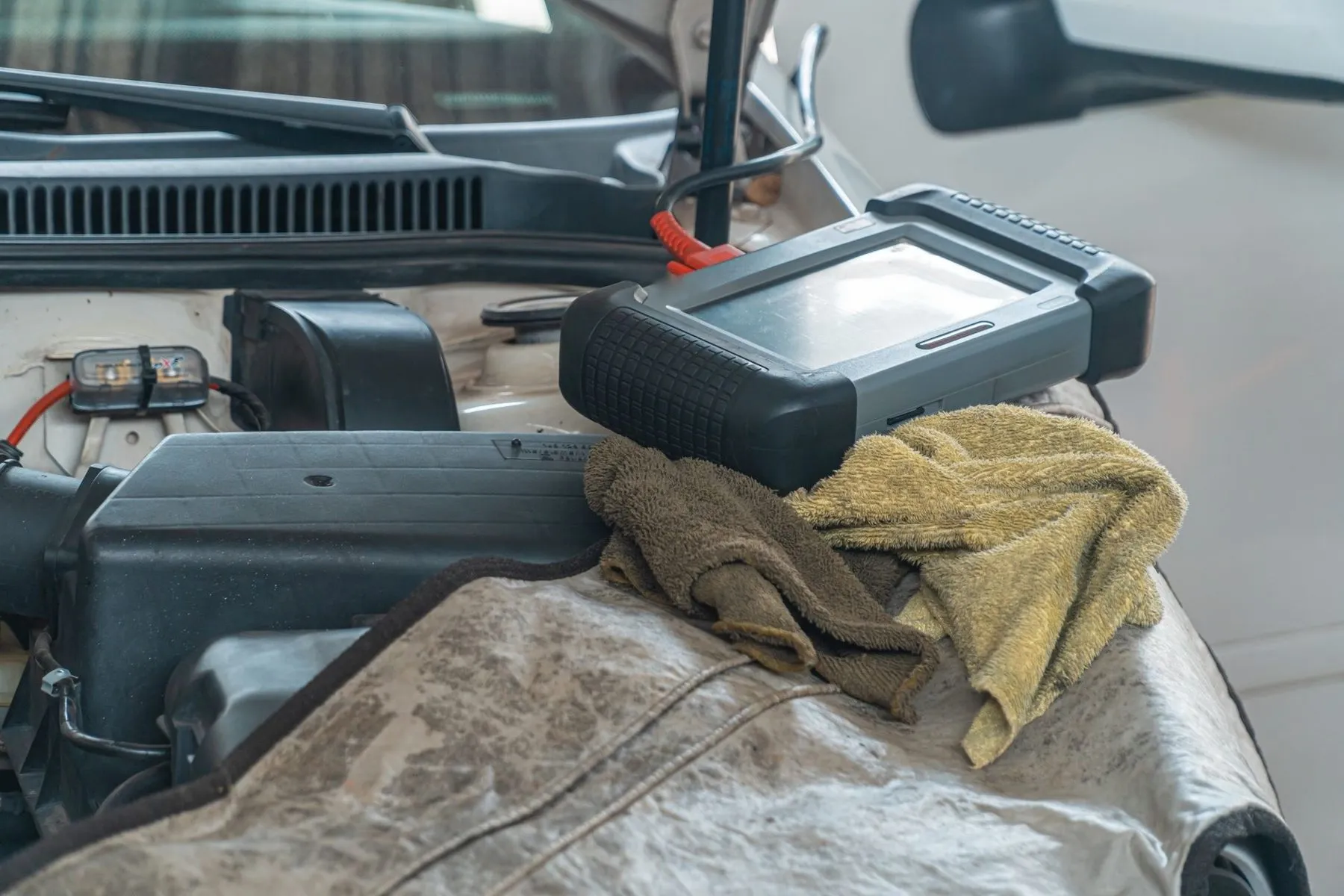 A diagnostic scanner resting on a cloth on the wing of a car with the bonnet open