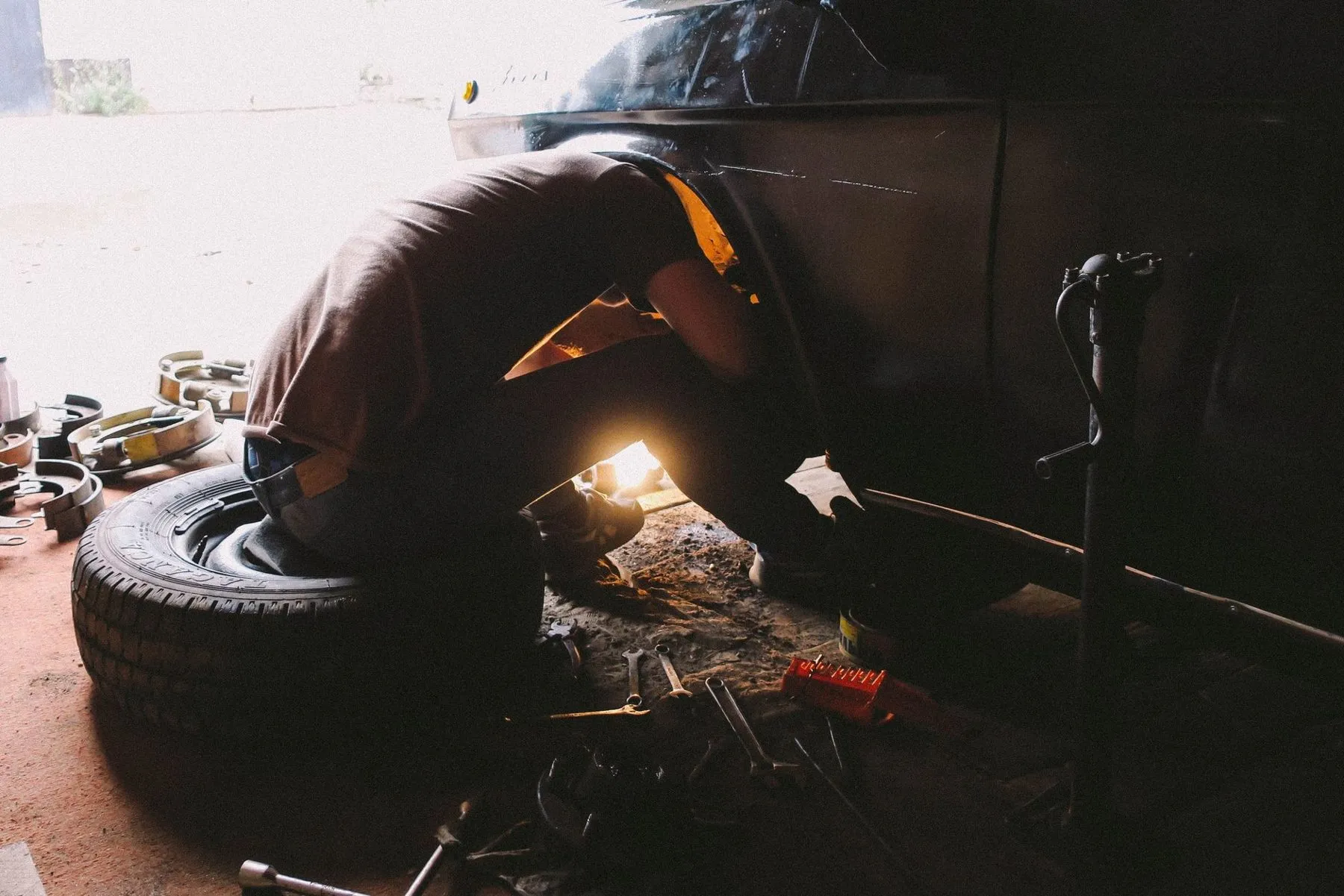 A technician crouched at a car's wheel arch with a work lamp